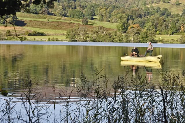Two anglers fishing from a boat on the calm waters of Butterstone Loch with wooded hills behind