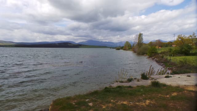 The Ebro river merging into the reservoir in the Orzales area, green hillsides reflected in calm water.