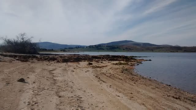 The Ebro reservoir seen from the sandy beach at Arija, with calm water and green slopes beyond.