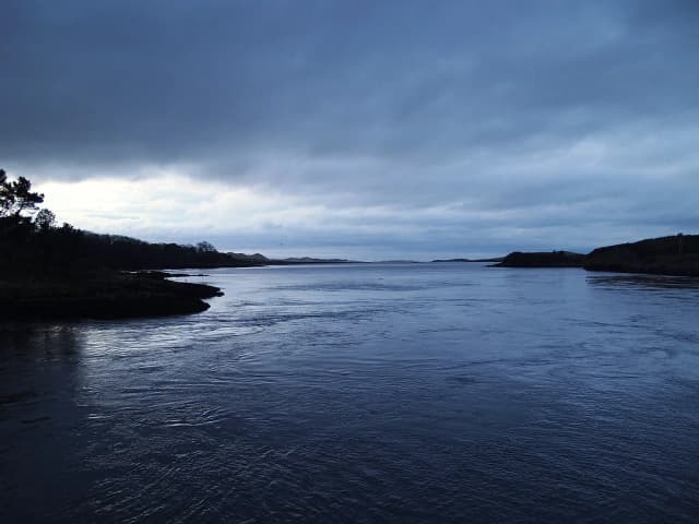 Wide, calm tidal waters of the River Erne estuary at Ballyshannon, Co. Donegal, Ireland, under a moody dusk sky.
