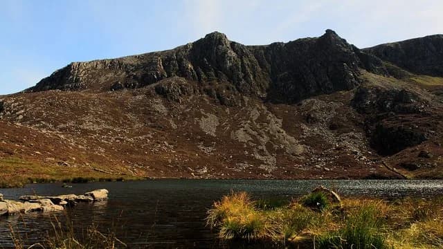 A dark corrie lake at Cwm Silyn with the crags of Craig yr Ogof rising behind it, Snowdonia.