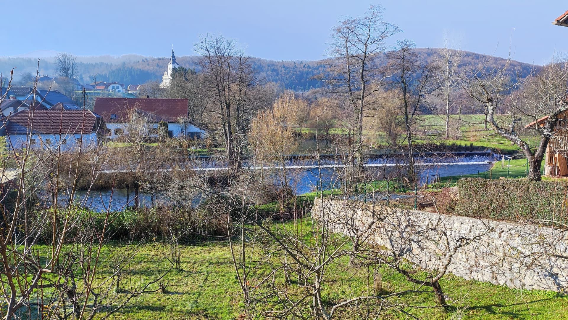 The Krka river flowing through Krka village, Slovenia, clear water over a stony bed and tree-lined banks.