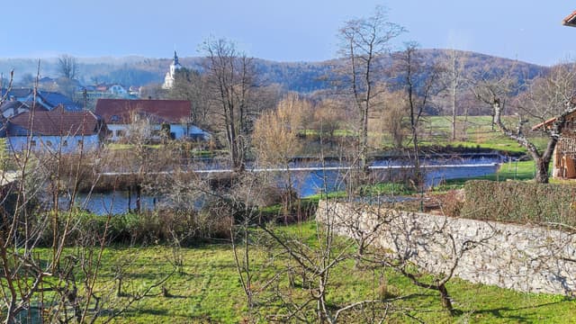 The Krka river flowing through Krka village, Slovenia, clear water over a stony bed and tree-lined banks.