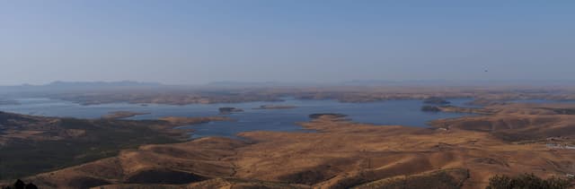 Wide panoramic view across the open water of La Serena reservoir with dehesa shoreline.