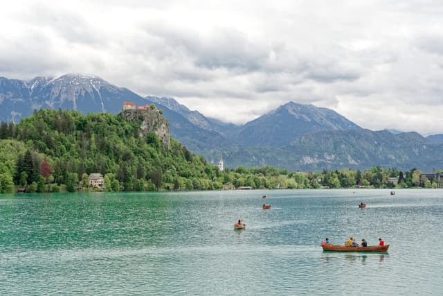 Wide shoreline view of Lake Bled with the lake in the foreground and Bled Castle on the cliff above the far shore.