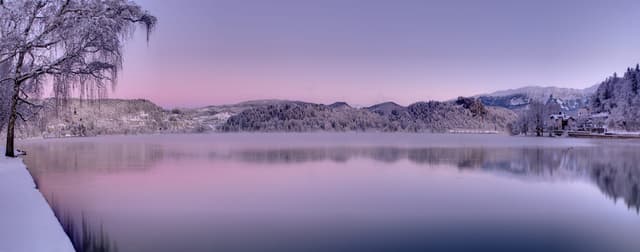 Wide panoramic view of Lake Bled showing the full lake basin, the island church, hillsides and the Julian Alps.