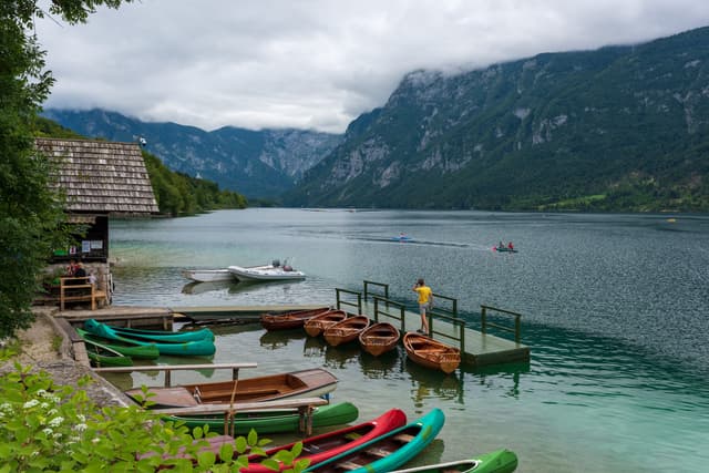 Boats and a wooden pier on Lake Bohinj at Ribčev Laz, mountain reflections on the calm water.