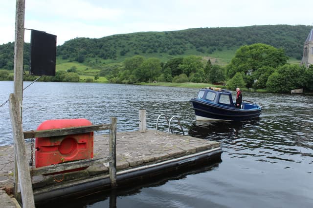 Wooden jetty at the Port of Menteith with the Inchmahome ferry on the open lake, tree-lined shoreline behind.