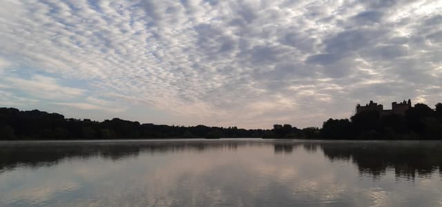 Wide panoramic view of Linlithgow Loch stretching across the frame under a partly cloudy sky, West Lothian.