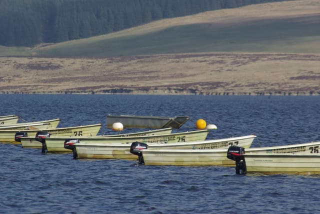 Fishing boats moored on the shore of Llyn Brenig reservoir with open water and moorland hills behind.