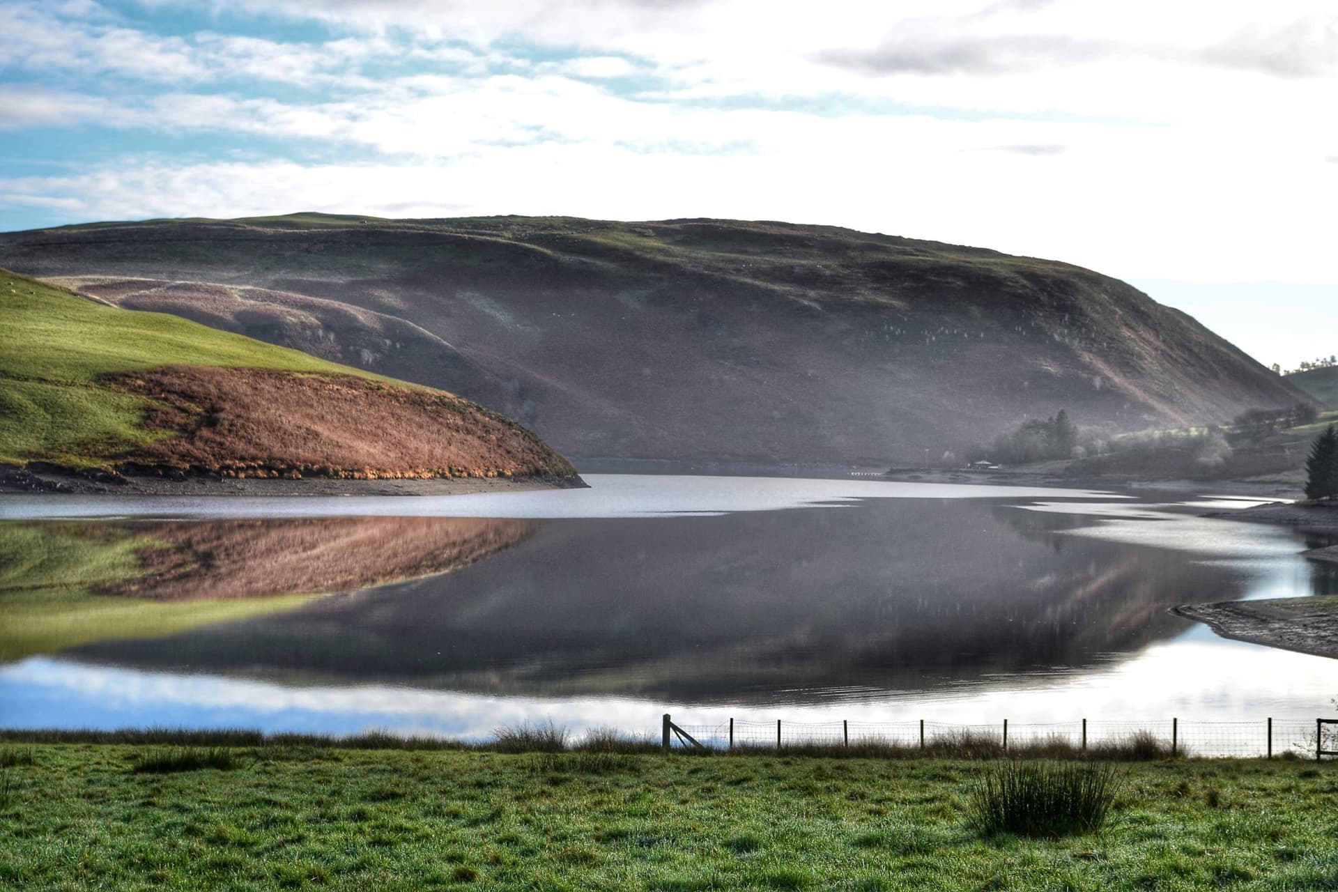 Clywedog dam with vivid reflections of autumn colour in the still reservoir water below.