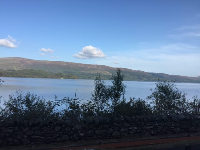 Open water of Loch Lomond north of Luss village, the western shoreline hills reflected in the calm surface.