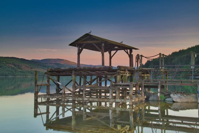 Wide view of Loch Tay at its western end under a golden sunset sky, still water reflecting the evening light.