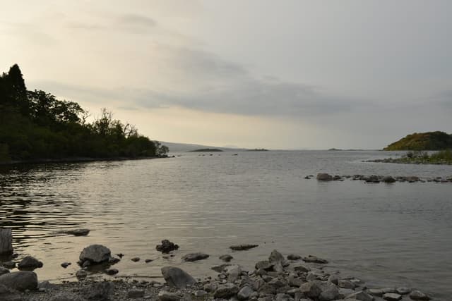 Rocky shoreline of White Island on Lough Mask at evening, calm water reflecting sunset light.