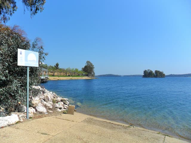 Dock and beach at Orellana reservoir with open water and moored boats, the only inland Blue Flag beach in Spain.