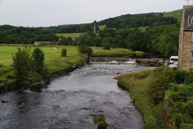 The River Ribble running over limestone ledges and shingle at Settle with the Dales skyline behind.