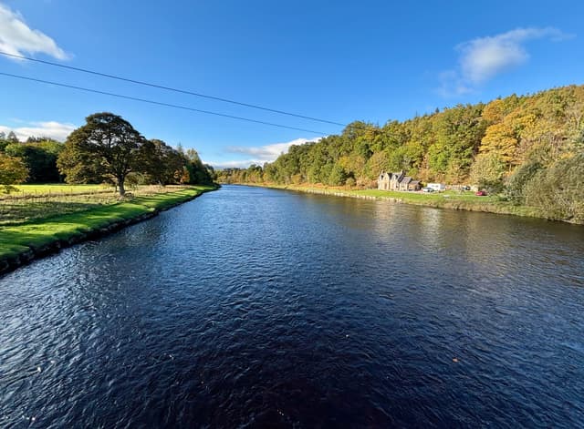 The River Spey at Aberlour viewed looking upstream, the river filling the frame with wooded valley sides beyond.