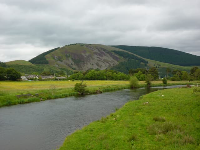 The River Tweed flowing through a wooded reach at Innerleithen in the upper Scottish Borders, summer greenery on the banks.