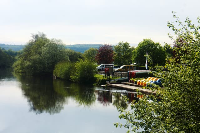 Rowing boats and trees reflected in the clear River Usk at Brecon, with the Brecon Beacons hills beyond.