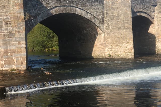 A small cascade and broken white water on the River Usk below Crickhowell Bridge, ducks resting on the river.