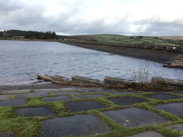 The concrete dam wall at the eastern end of Usk Reservoir with the reservoir water behind the structure.