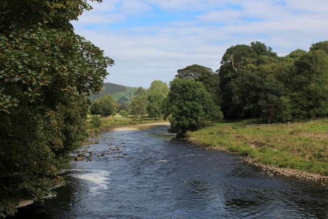 The River Wharfe flowing through a wide gravel-bed channel at Bolton Abbey with tree-lined banks.